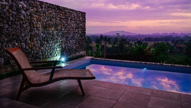 Un muro de piedra, una silla de salón y una piscina con vistas a colinas distantes.