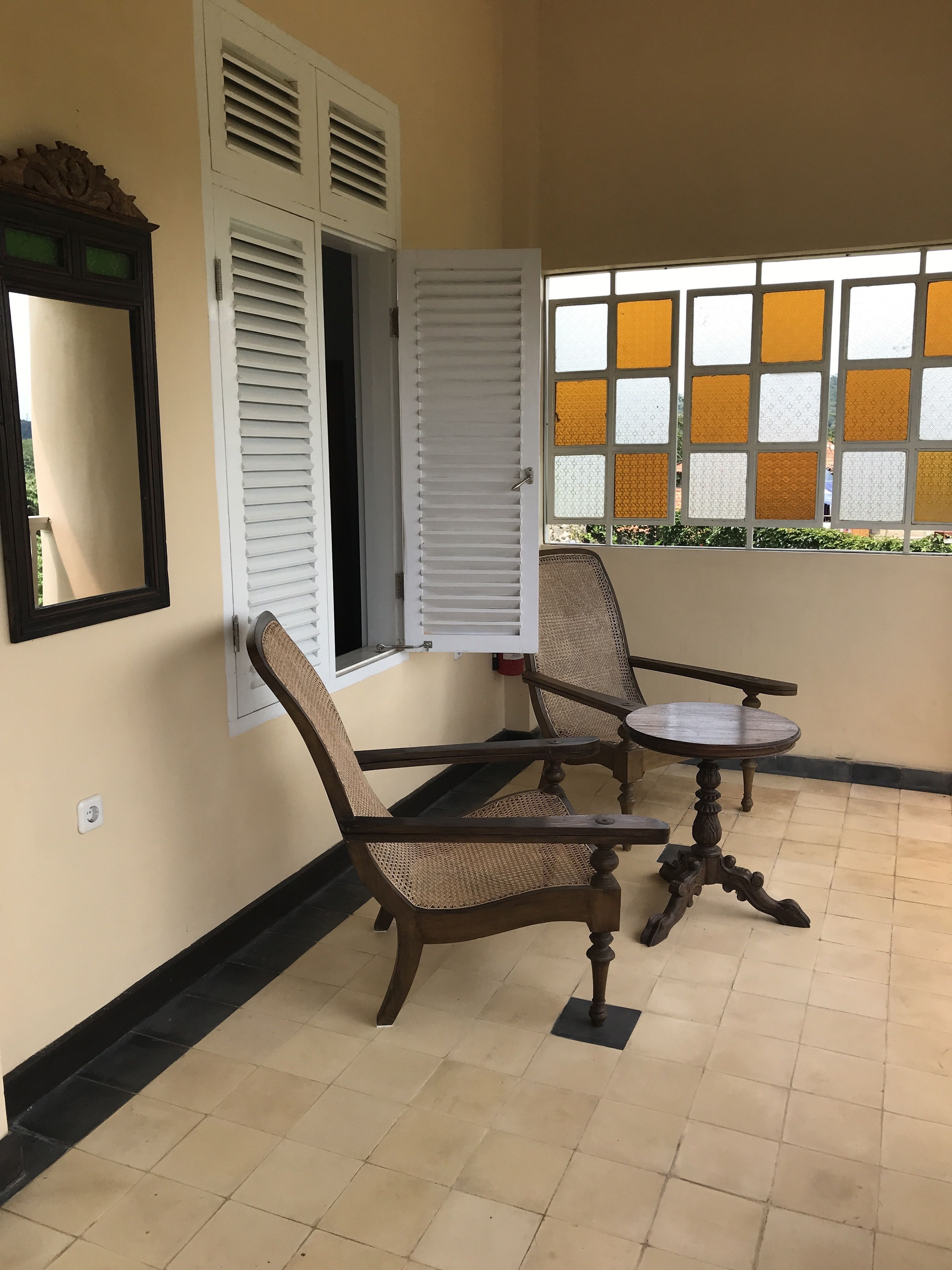 A room with a window, a chair, a table, and a mirror.