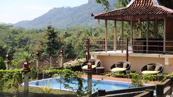 Zona de piscina con sillas de descanso y un pabellón con vistas a un paisaje montañoso.