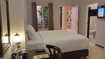 A hotel room with a bed, a table with a kettle, a remote control, and a television on the wall.