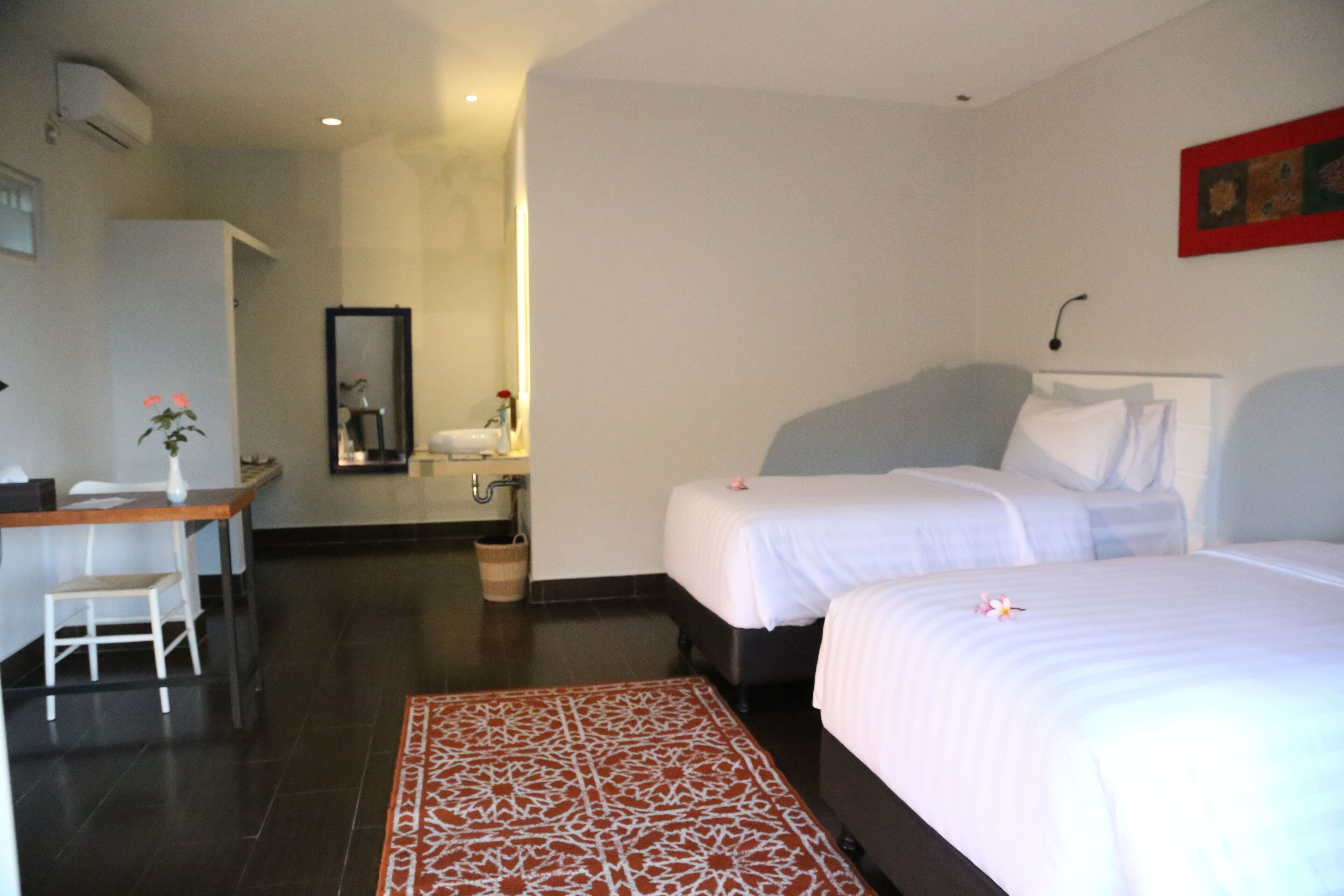 Une chambre d’hôtel avec deux lits, un bureau, une chaise, une salle de bain et un tapis à motifs.
