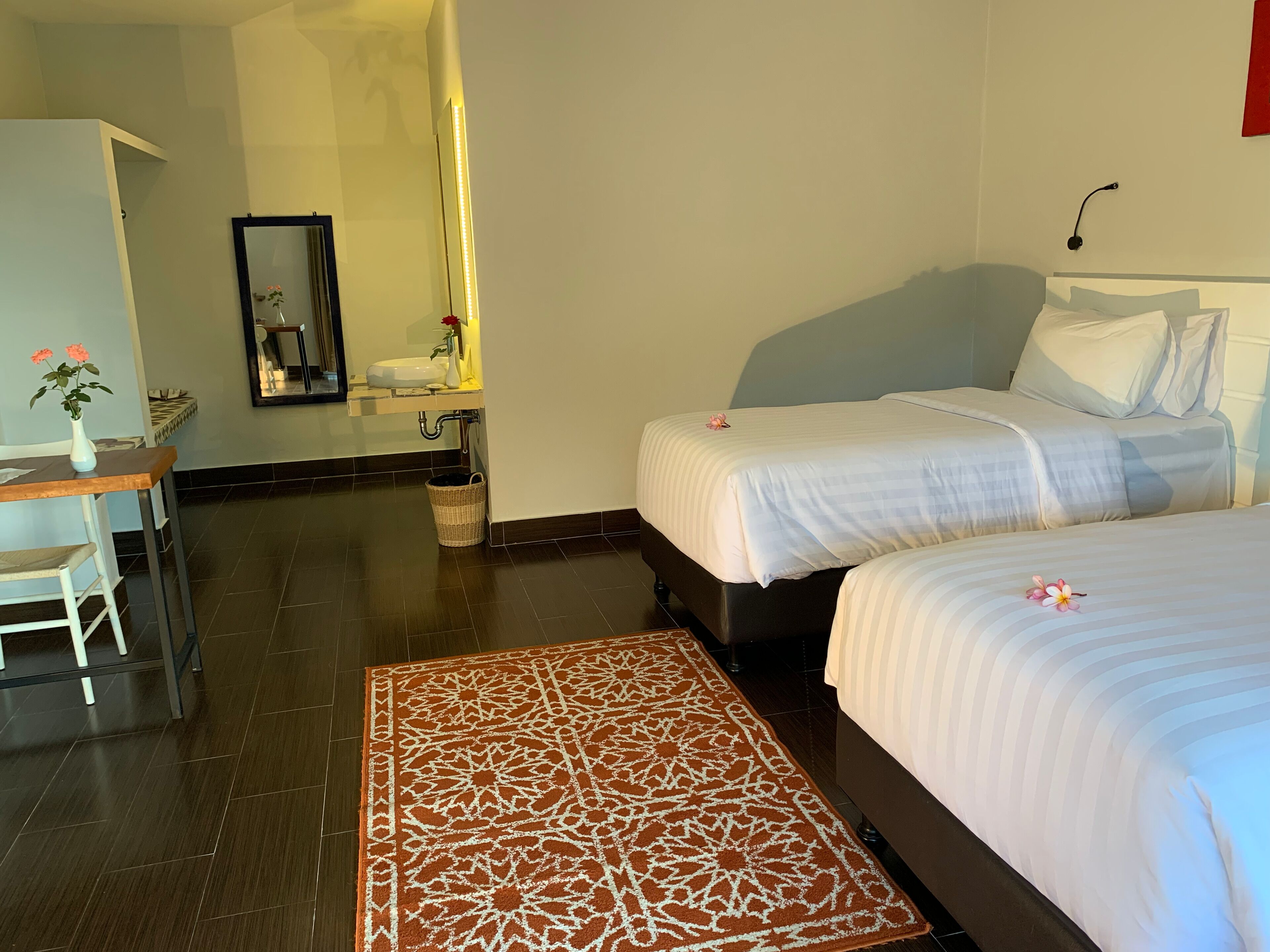 A hotel room with two beds, a desk, a bathroom, and a patterned rug.