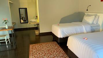 A hotel room with two beds, a desk, a bathroom, and a patterned rug.