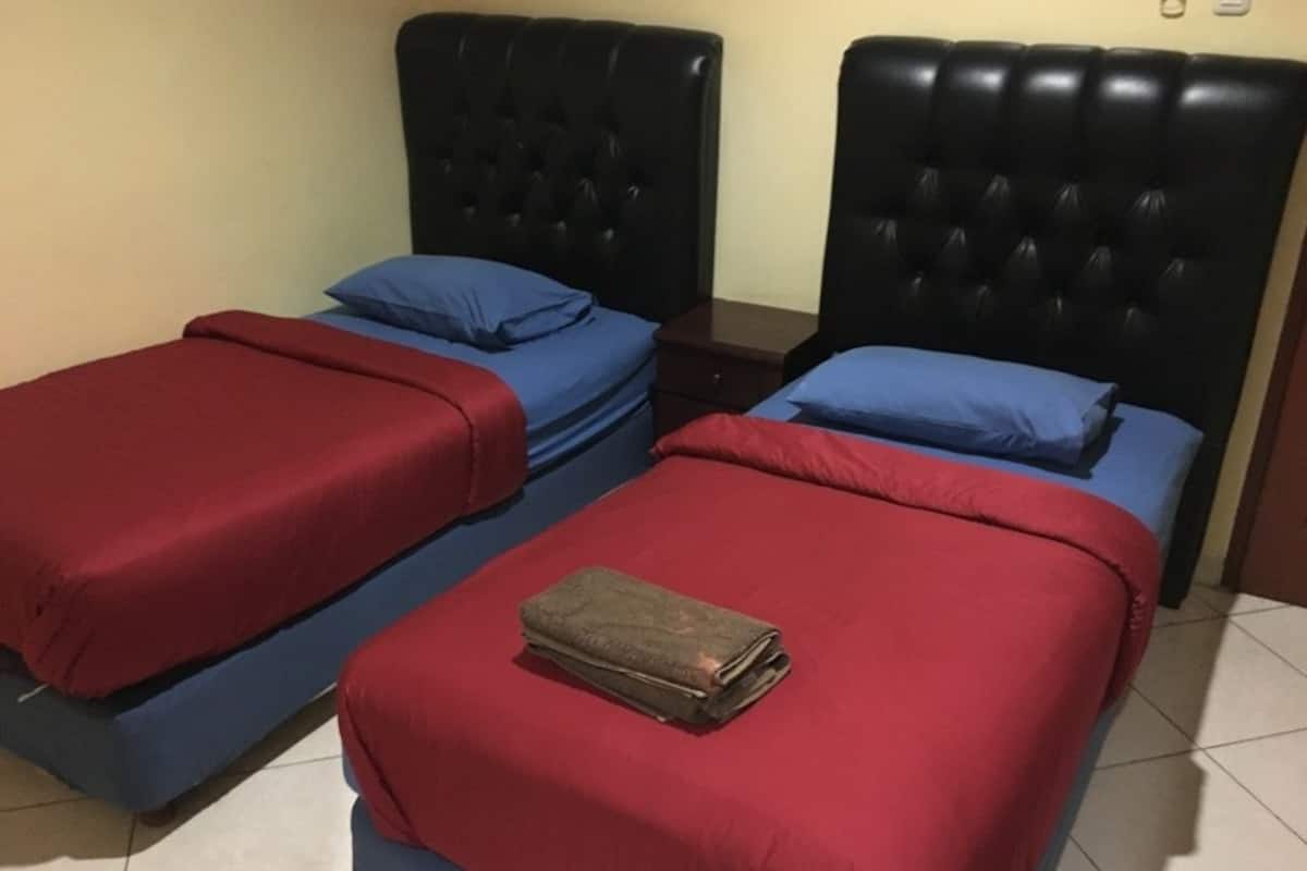 Dos camas con ropa de cama roja y azul, una toalla doblada en la cama en primer plano y un cabecero oscuro.