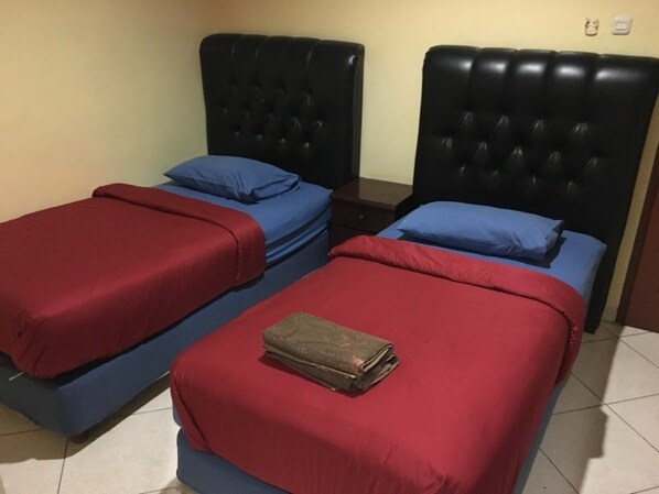 Dos camas con ropa de cama roja y azul, una toalla doblada en la cama en primer plano y un cabecero oscuro.