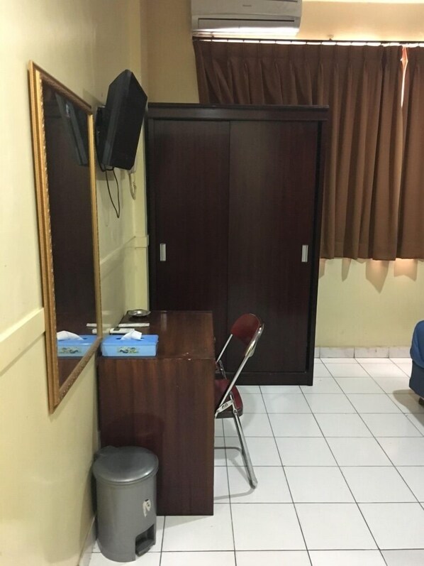 A room with a wooden desk, a chair, a mirror, a wardrobe, a trash bin, and a curtain. - Hotel Aceh Besar (Jakarta)