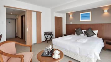 A hotel room with a large bed, a wooden chair, a small table with glasses and cups, and a painting on the wall.