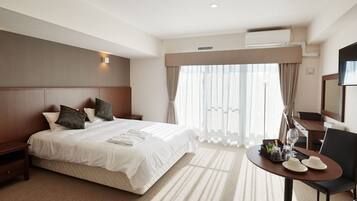 Quarto de hotel com uma cama grande, uma mesinha de cabeceira, uma escrivaninha com cadeira e uma televisão.