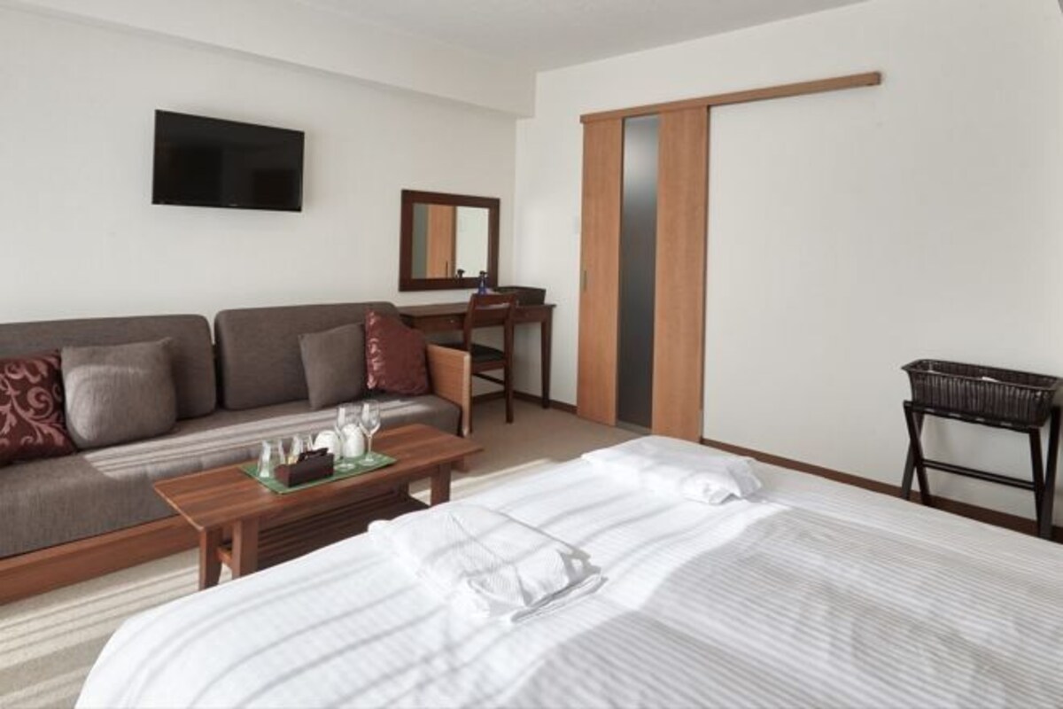 A hotel room with a bed, a sofa, a desk, a television, and a wardrobe.