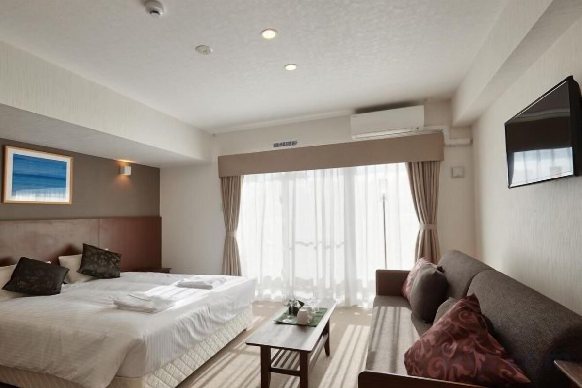 Quarto de hotel com cama, sofá, mesa e televisão.