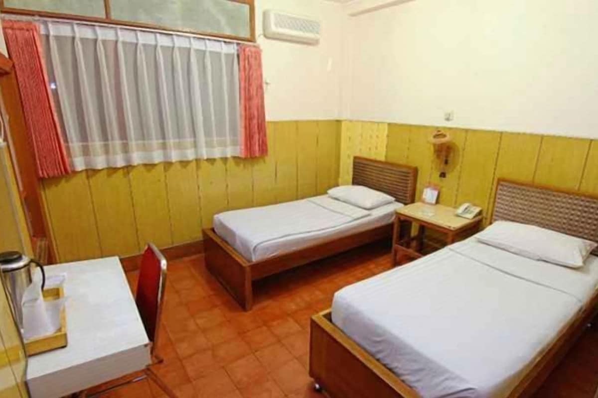 A small, single-room accommodation with two single beds, a desk, and a chair.