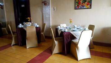 A dining area with tables set for four, each with a vase of flowers, chairs, and a tiled floor.