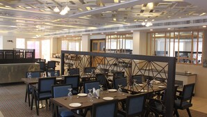 A restaurant with a modern ceiling design, multiple tables set for dining, and a view of the city through large windows. - Maya Heritage (Gaya)