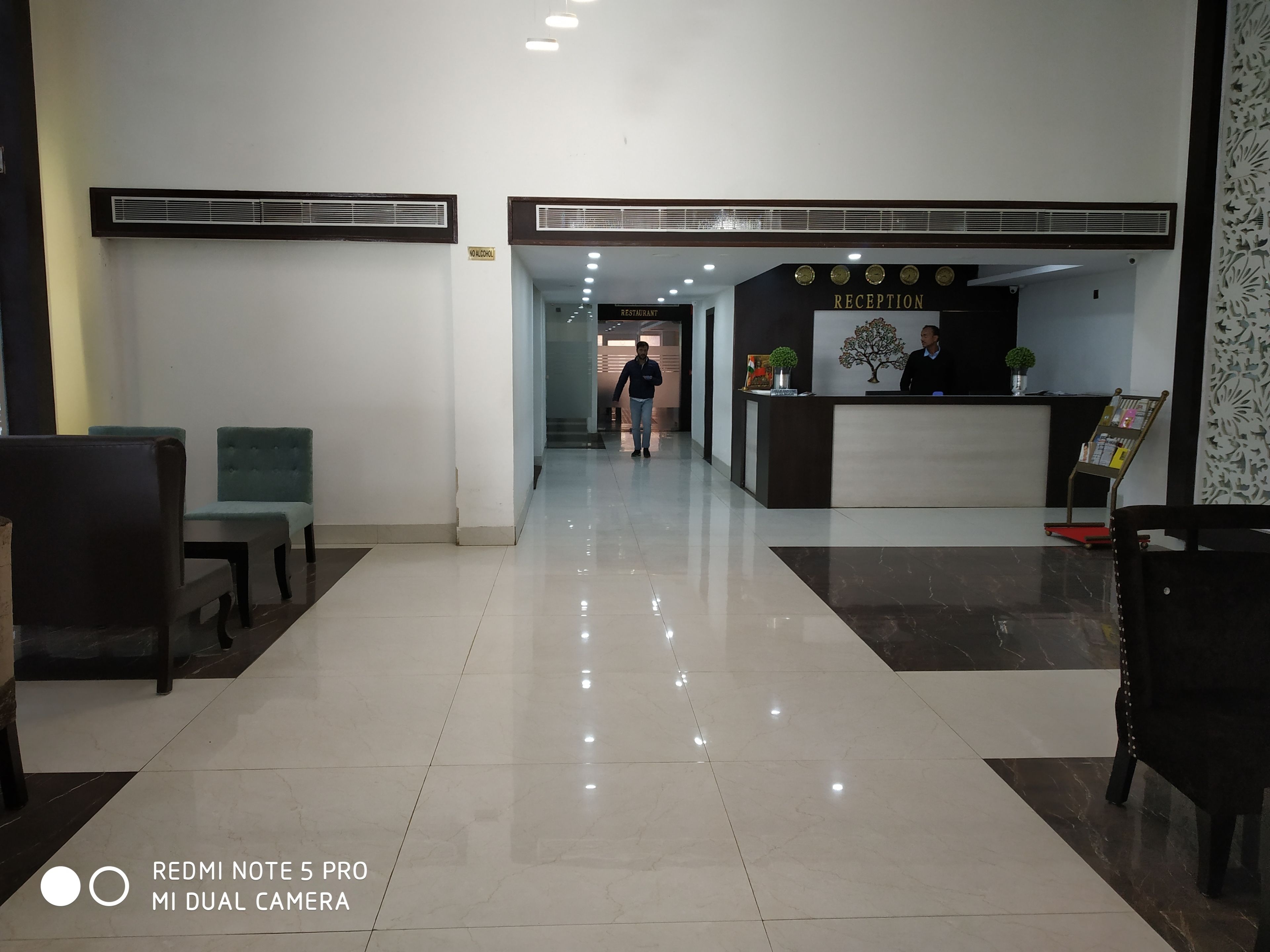 A hotel reception area with a clean, tiled floor, a reception desk, and a sign indicating a restaurant.