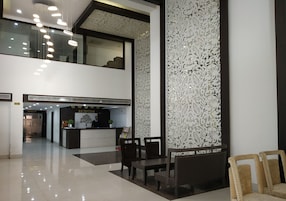 Zona de recepción de un hotel con mostrador, sillas y una escalera que lleva a un nivel superior.