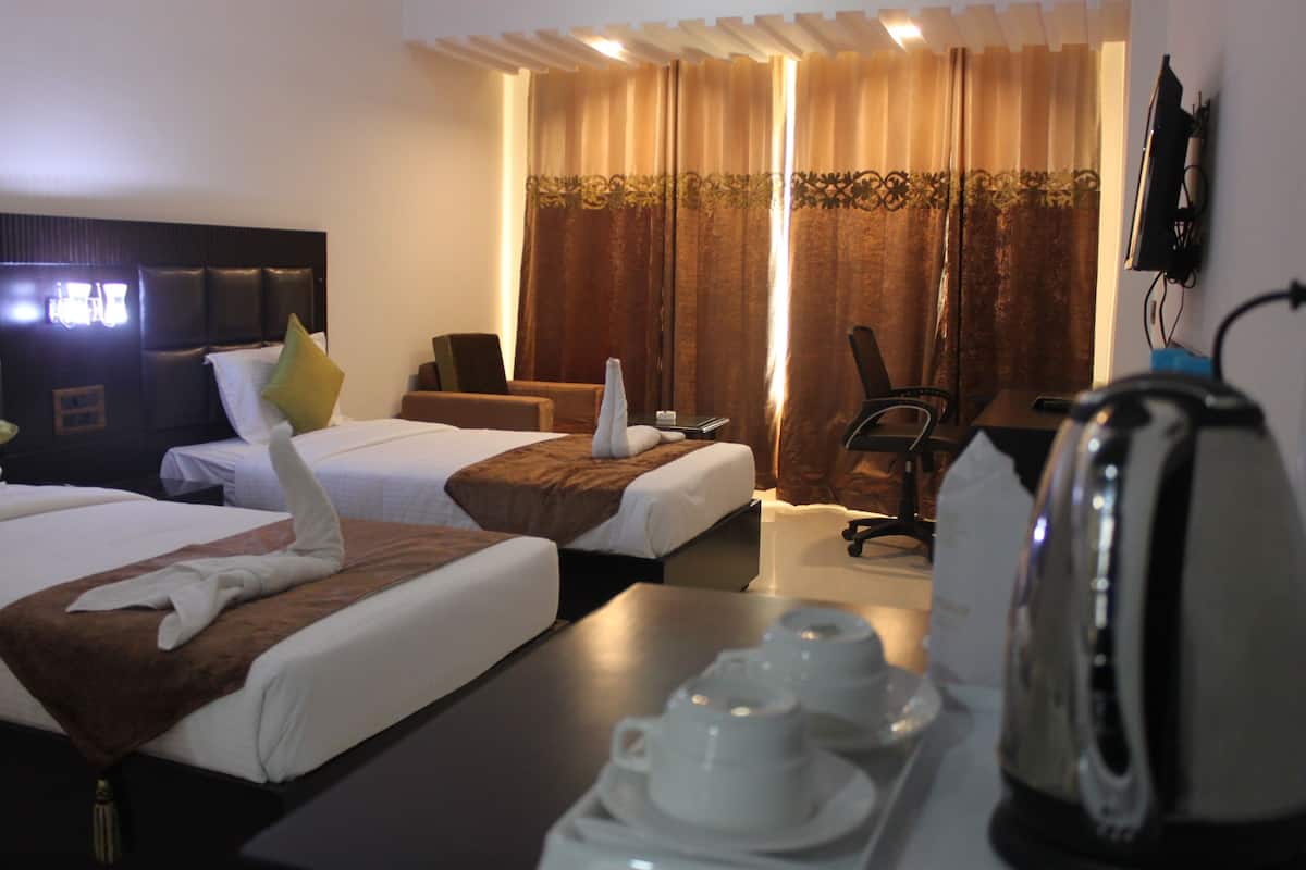 A hotel room with two beds, a desk, a chair, a television, and a kettle.