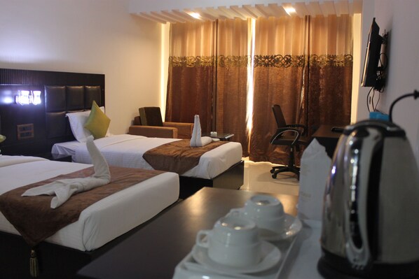 A hotel room with two beds, a desk, a chair, a television, and a kettle. - Maya Heritage (Gaya)