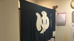 Una habitación con una cortina azul oscuro que tiene un gran símbolo blanco, un reloj en la pared y un cartel que indica los horarios de la ducha.