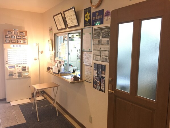 Un espace d’accueil comprenant un distributeur de billets, une petite table et divers panneaux d’affichage au mur.