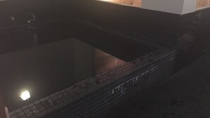 Una bañera oscura con revestimiento de azulejos, desagüe visible y reflejos de luz en el agua.