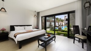 Une chambre d’hôtel moderne avec un grand lit, une petite table avec des fruits, une chaise et une vue sur une piscine.