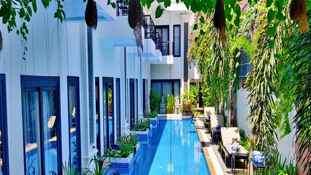 Un hôtel moderne doté d’une longue piscine, entouré d’une végétation luxuriante et surplombant un ciel d’un bleu limpide.