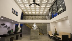 Un hall d’entrée moderne avec une statue centrale, un comptoir d’accueil, un espace salon et un escalier.