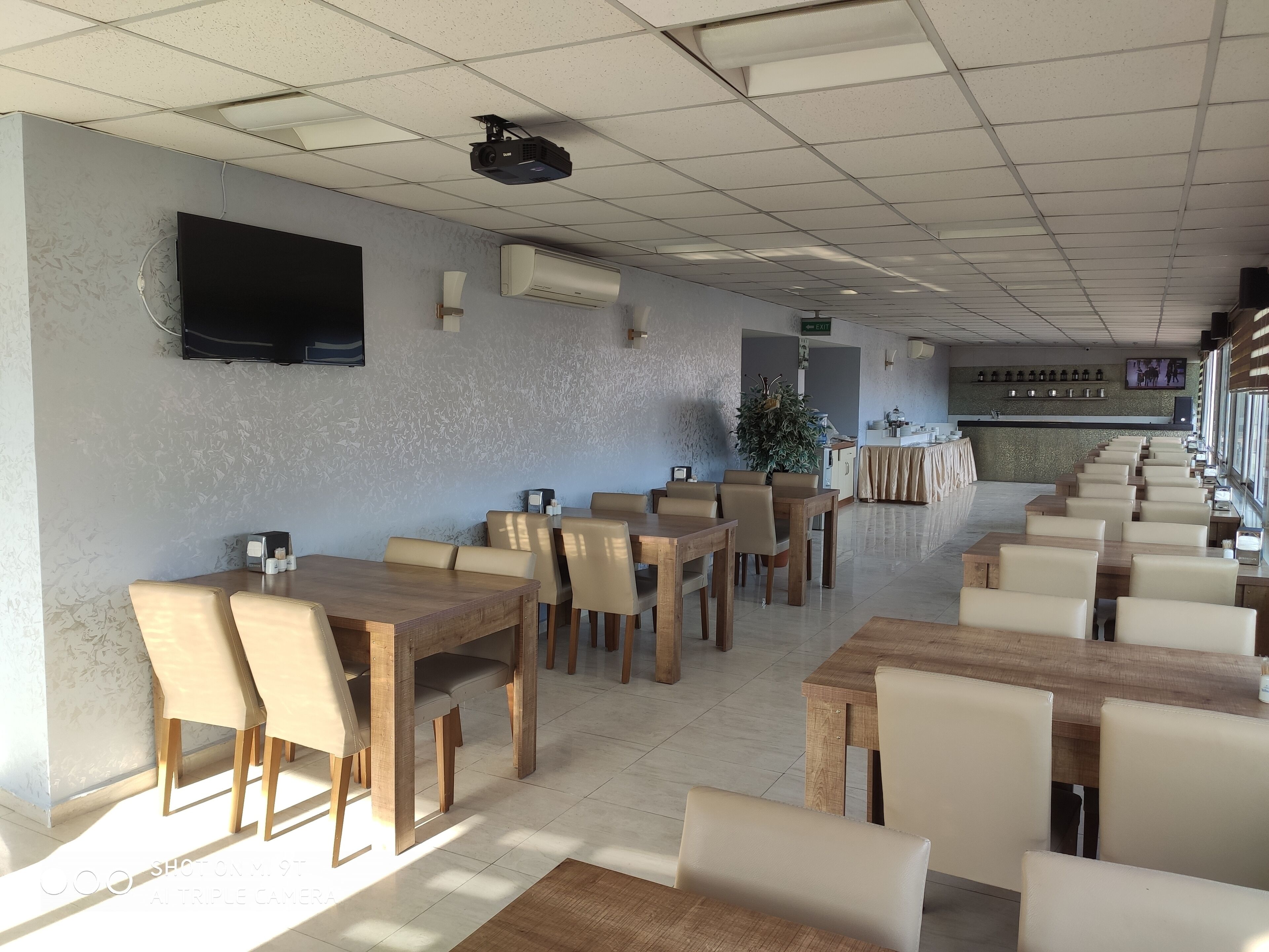 Un restaurante espacioso con varias mesas y sillas de madera, un televisor de pantalla plana en la pared y un equipo de aire acondicionado.