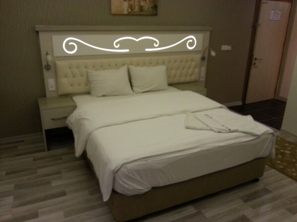 A neatly made bed with white linens, a wooden nightstand, and a wall-mounted light fixture.