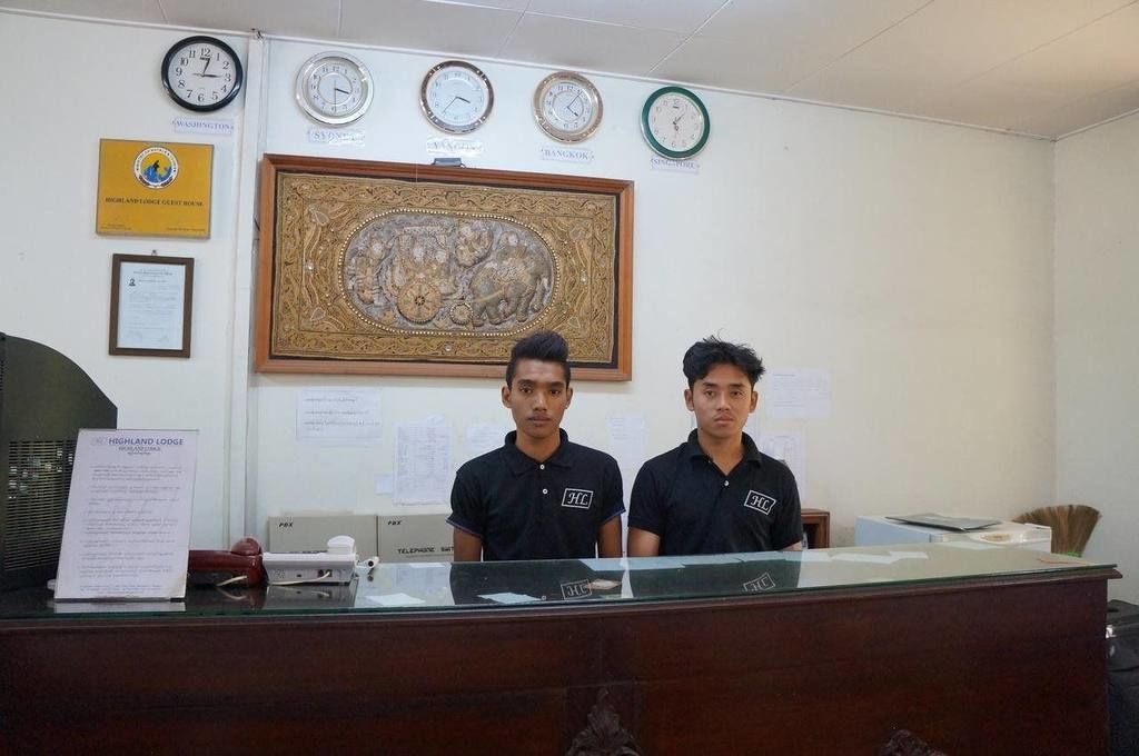 A reception desk with two individuals standing behind it, a clock, framed artwork, and various certificates on the wall.