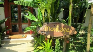 A wooden sign with the word "montage" in gold lettering, surrounded by lush greenery and a wooden structure. - Highland Lodge Hotel (Yangon)
