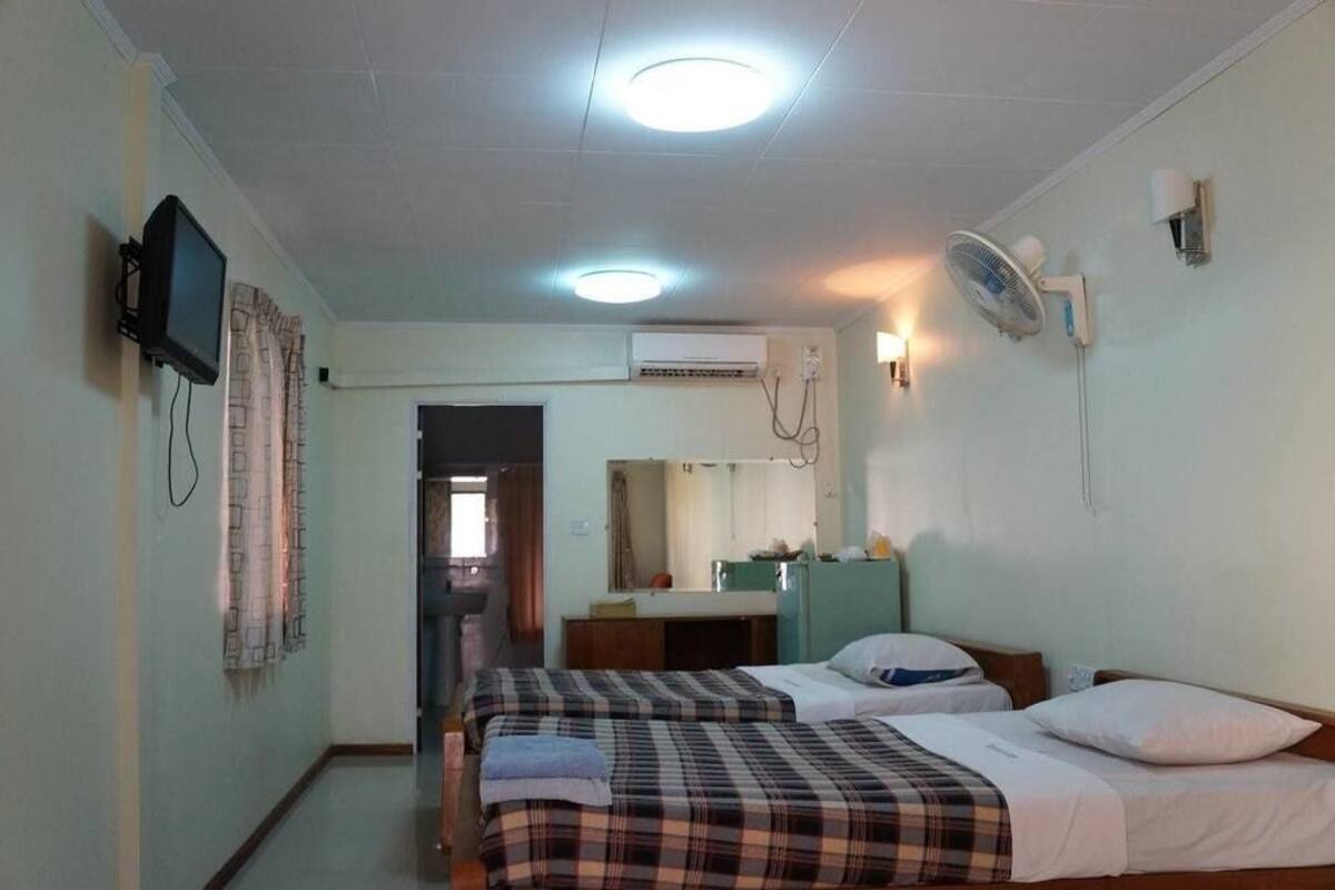 A hotel room with two beds, a television, an air conditioning unit, a mirror, and a fan.