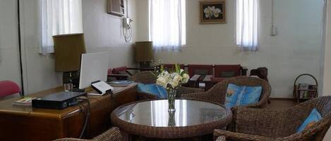 A room with a round dining table, wicker chairs, a sofa, and a chandelier.