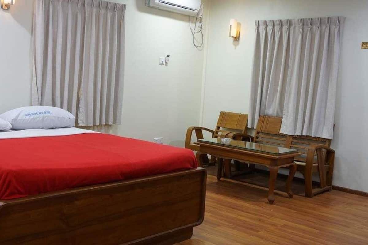 A hotel room with a wooden bed, a red bedspread, two white pillows, a wooden table with chairs, and a 'No Smoking' sign on the wall.