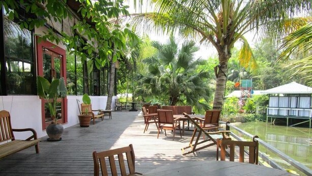 A wooden deck with outdoor seating, surrounded by lush greenery and a water body. - Highland Lodge Hotel (Yangon)