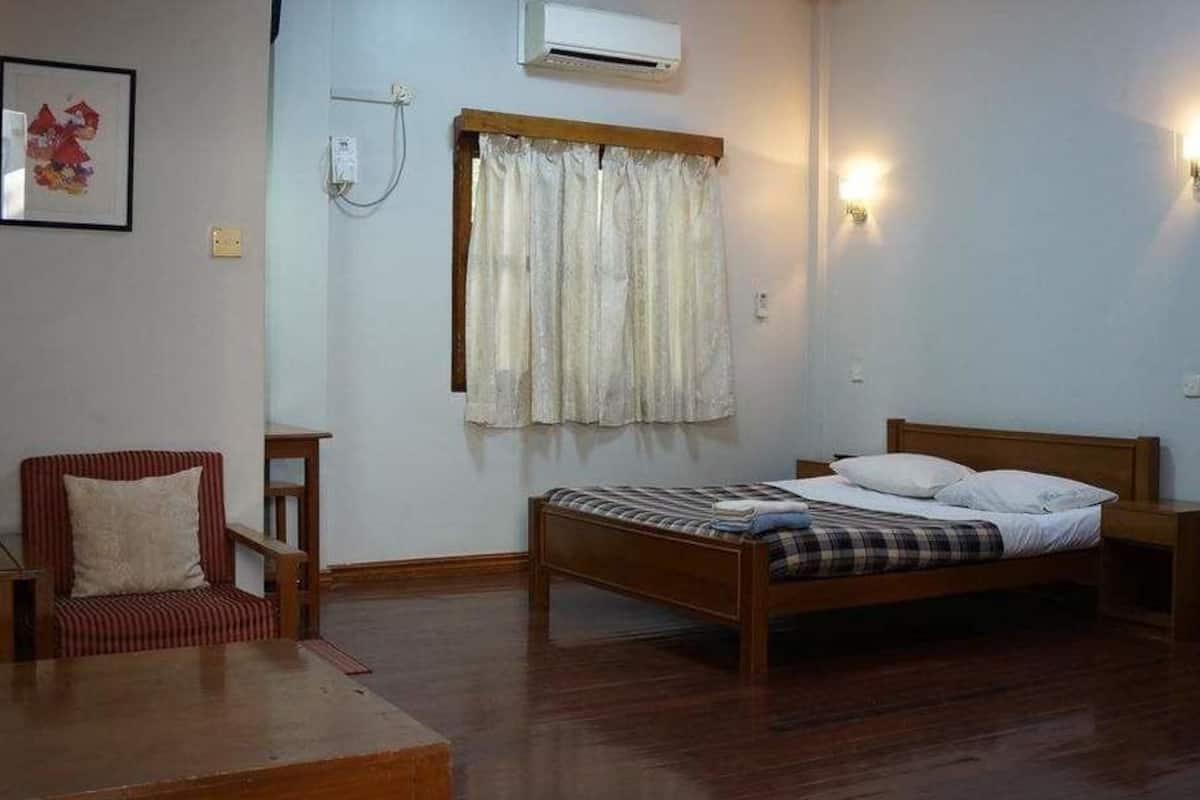 A bedroom with a wooden bed, a chair, a wardrobe, and a wall-mounted air conditioner.