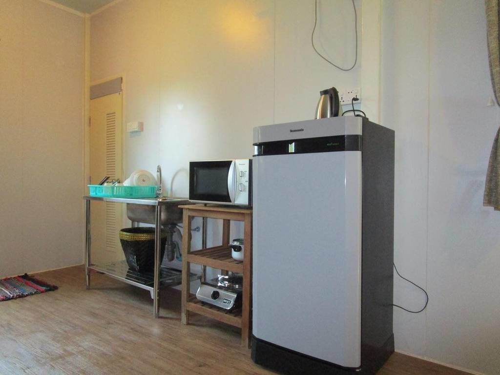 A compact kitchen with a refrigerator, microwave, and a small table with a basket and a kettle.