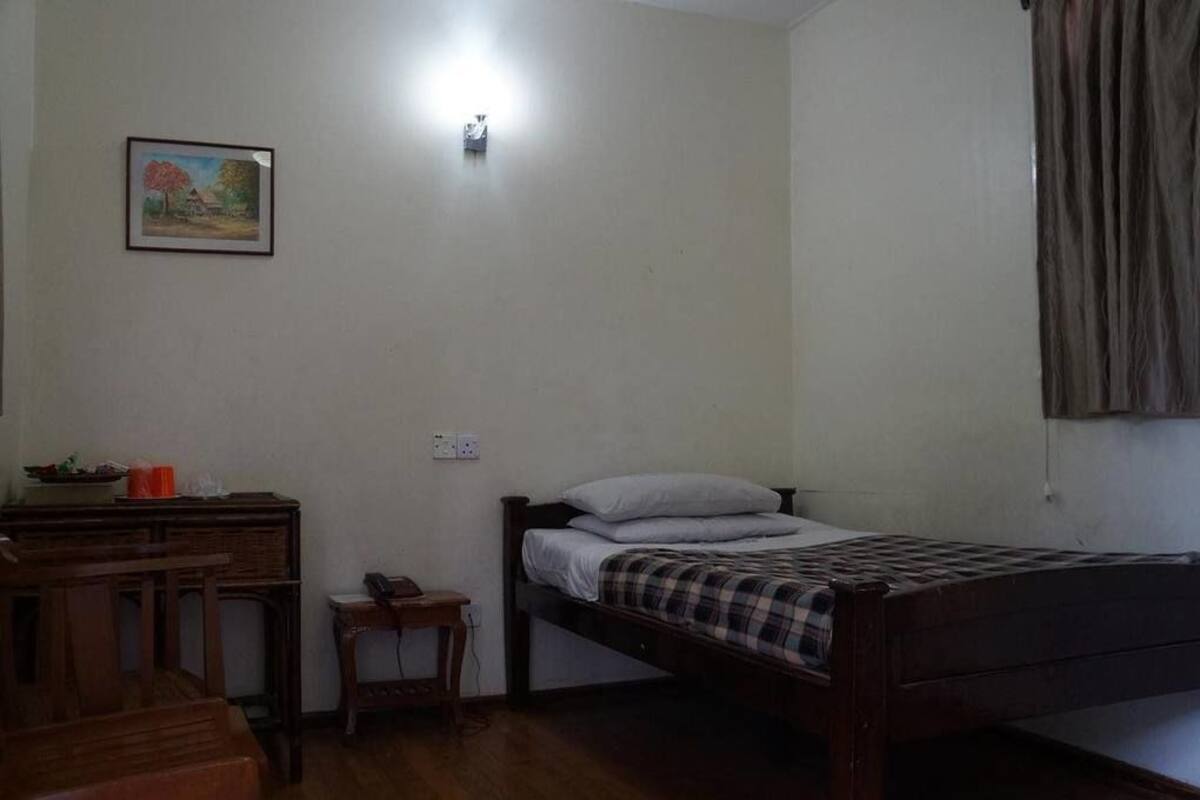 A small, sparsely furnished room with a single bed, a desk, and a chair.