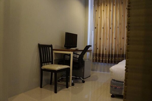 A hotel room with a wooden chair, a desk with a computer, a bed, and a curtain. - Highland Lodge Hotel (Yangon)
