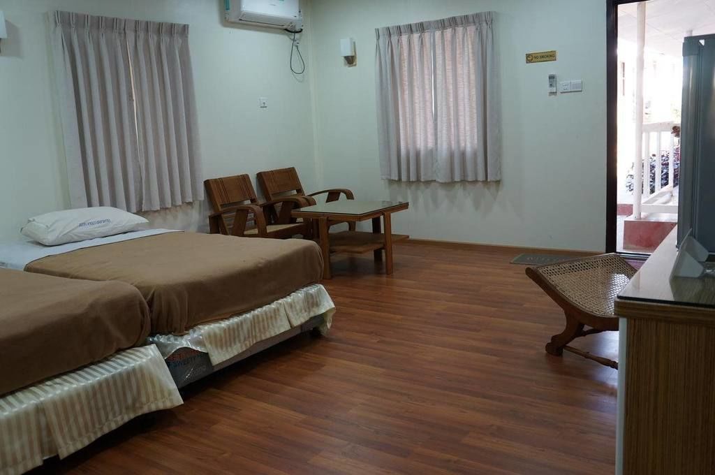 Una habitación de hotel con dos camas, una mesa de madera, dos sillas y un televisor.