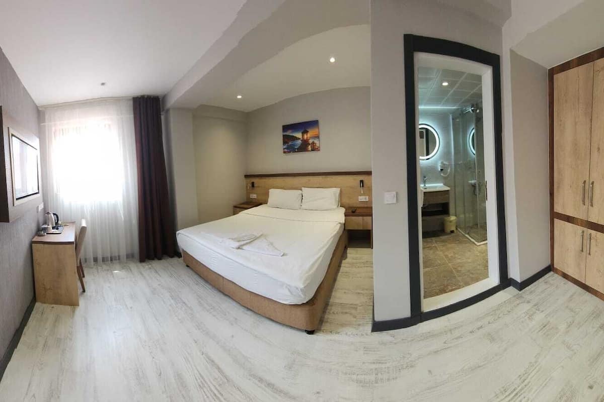 Una habitación de hotel moderna con cama, escritorio y baño visible a través de una puerta de cristal.
