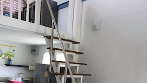 Une cuisine moderne avec un réfrigérateur en acier inoxydable, des armoires blanches et un plancher en bois. Un escalier en métal mène à un niveau supérieur.