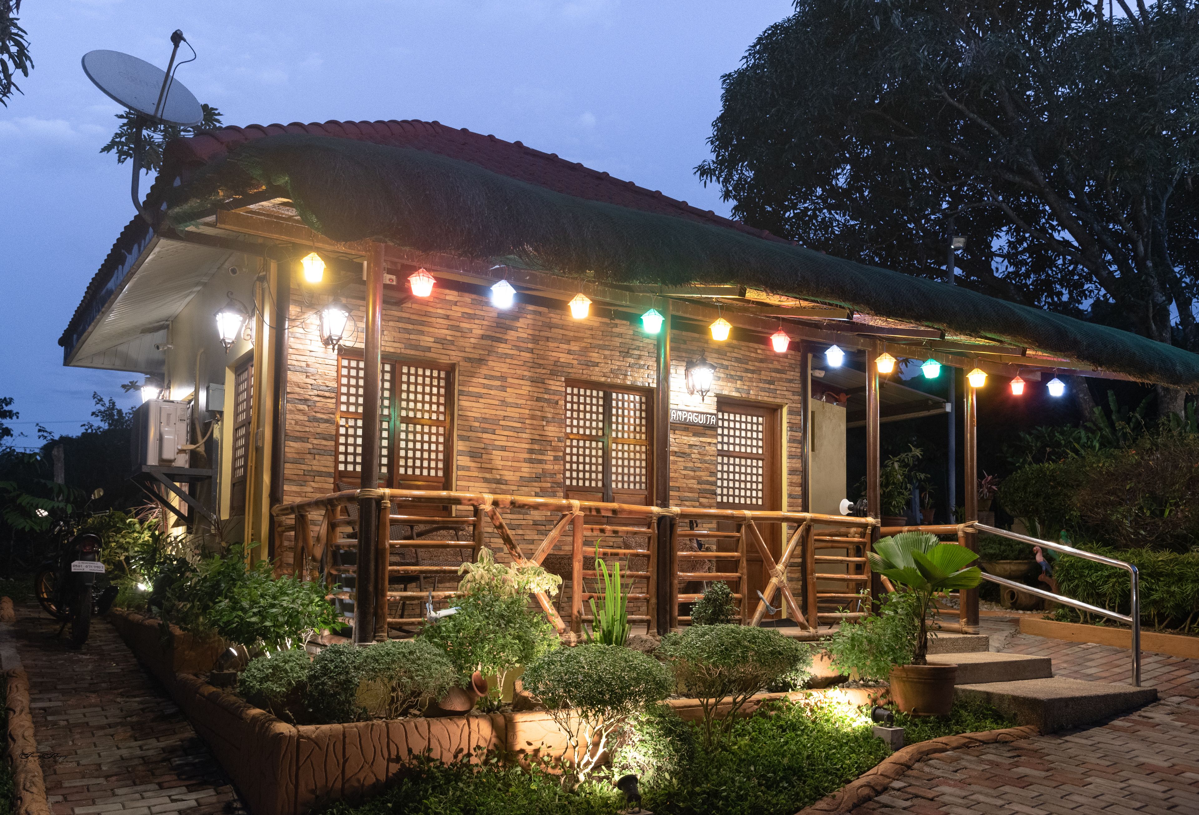 Una casa de madera rústica con techo de paja, rodeada de jardines cuidados y un sendero de ladrillo.
