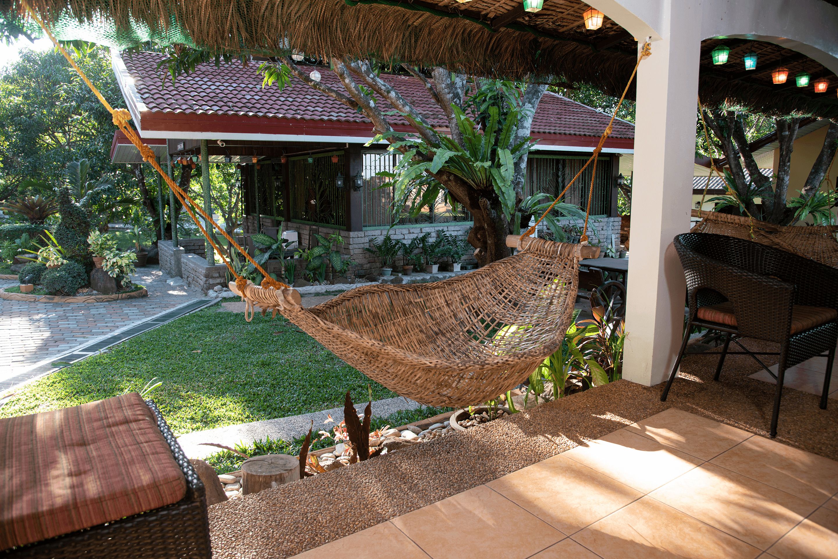 A hammock chair suspended over a garden area with a patio and outdoor seating.