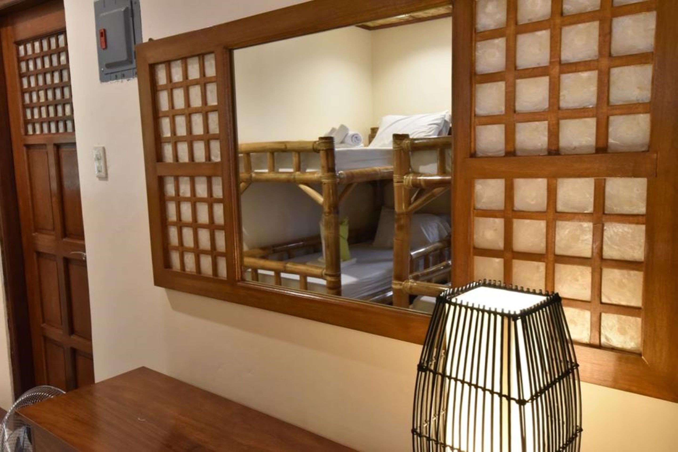 A room with a wooden bunk bed, a mirror with a wooden frame, and a black lamp on a wooden table.