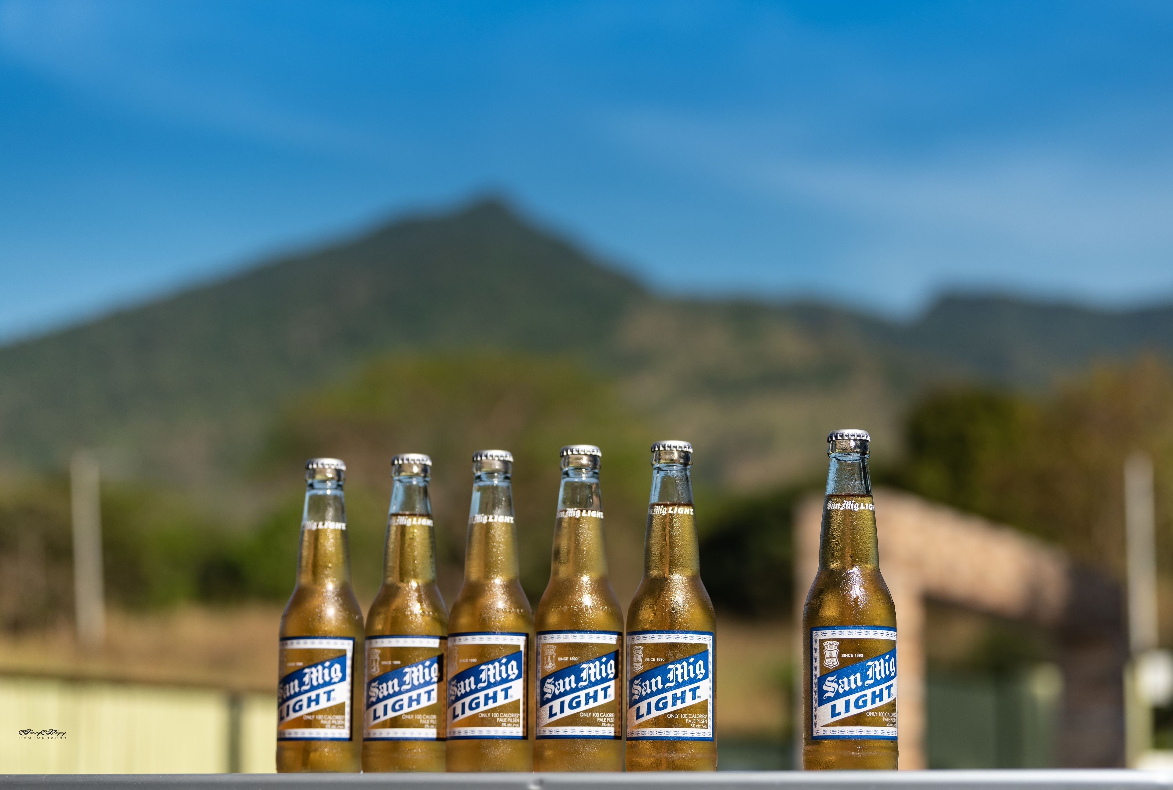 Six bottles of San Miguel Light beer on a ledge with a mountainous background.