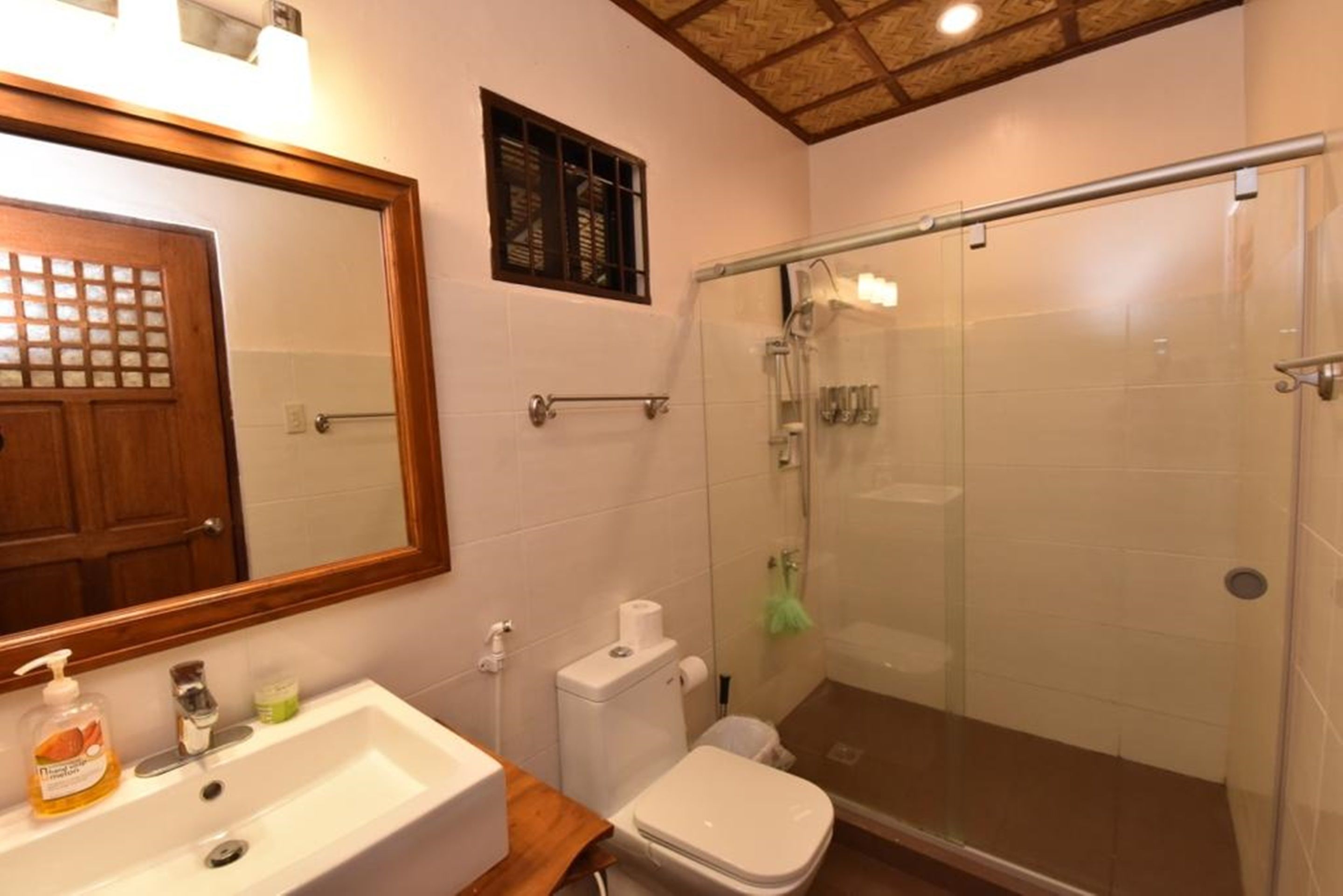 A bathroom with a wooden door, a white sink, a toilet, and a glass-enclosed shower area.