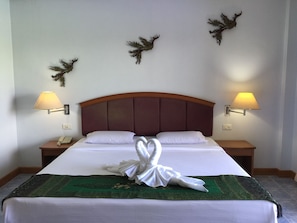 A neatly made bed with a green and white bedspread, two white pillows, and a towel arranged in a swan shape. There are two wall-mounted lamps on either side of the bed. - Krabi Golden Hill Hotel (Krabi)