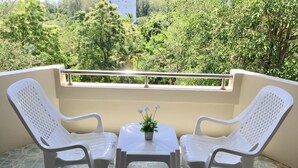 Un balcon avec deux chaises en plastique blanc et une petite table, un pot de fleurs et une rambarde.