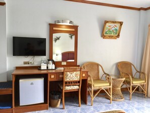 A hotel room with a wooden desk, a television, wicker chairs, a small refrigerator, and a wall-mounted picture. - Krabi Golden Hill Hotel (Krabi)
